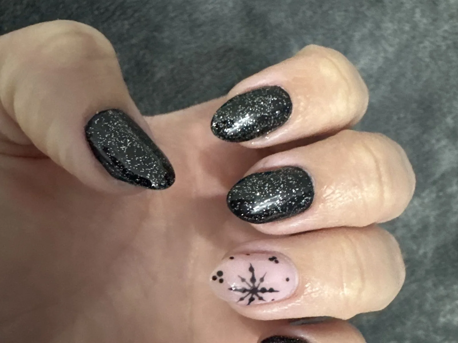 Uñas almendradas negras con brillo plateado y una uña nude con copo de nieve