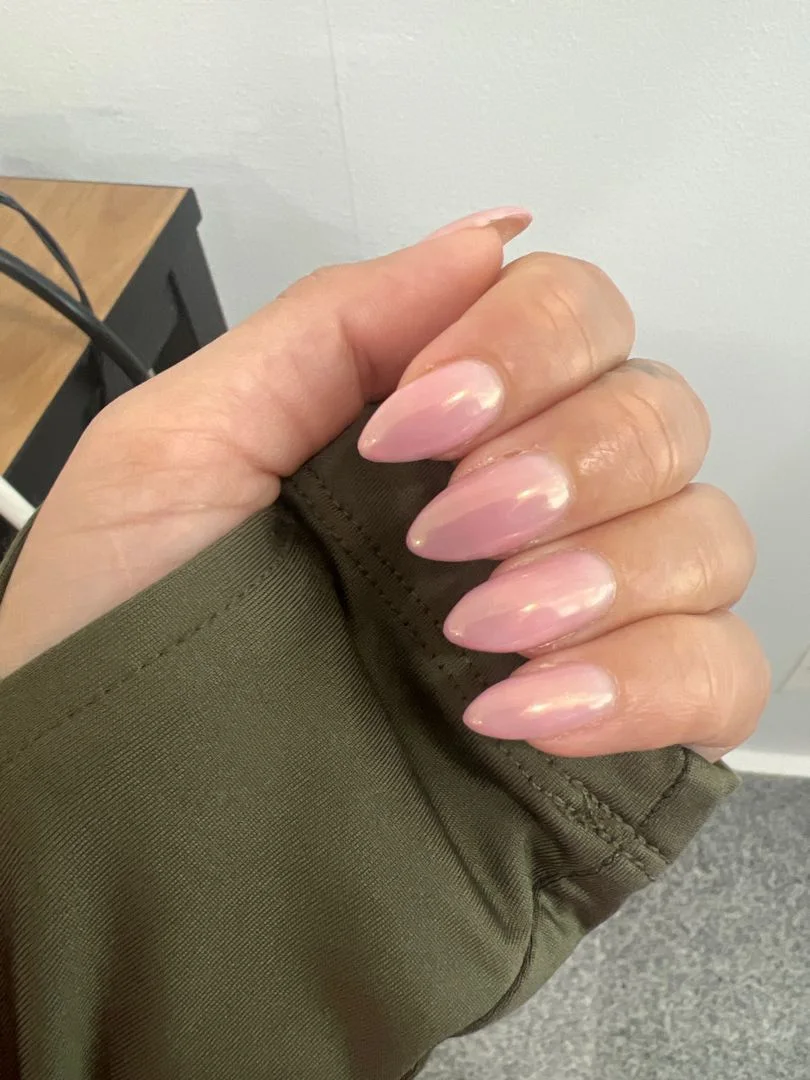 Mano con uñas almendradas rosa con efecto cromado perlado sobre manga verde