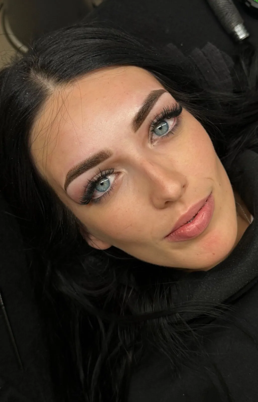 Primer plano de una clienta con cejas micropigmentadas, pestañas definidas y labios rosados