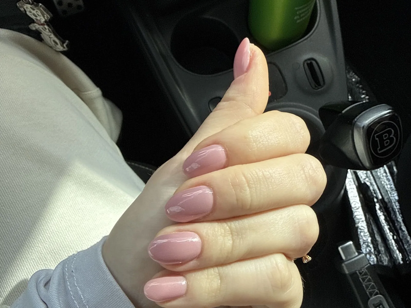 Mano en gesto de pulgar arriba con uñas ovaladas en rosa empolvado brillante