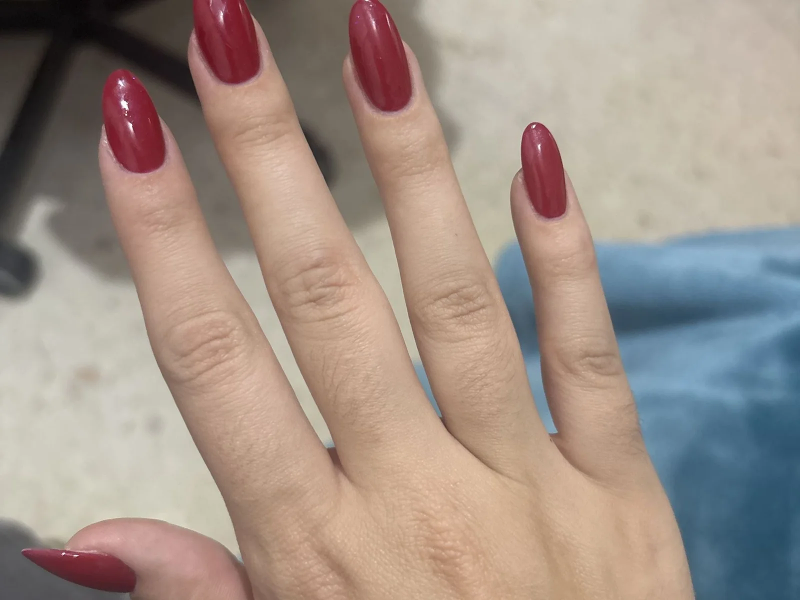 Mano con uñas almendradas largas en esmalte rojo burdeos brillante sobre fondo neutro