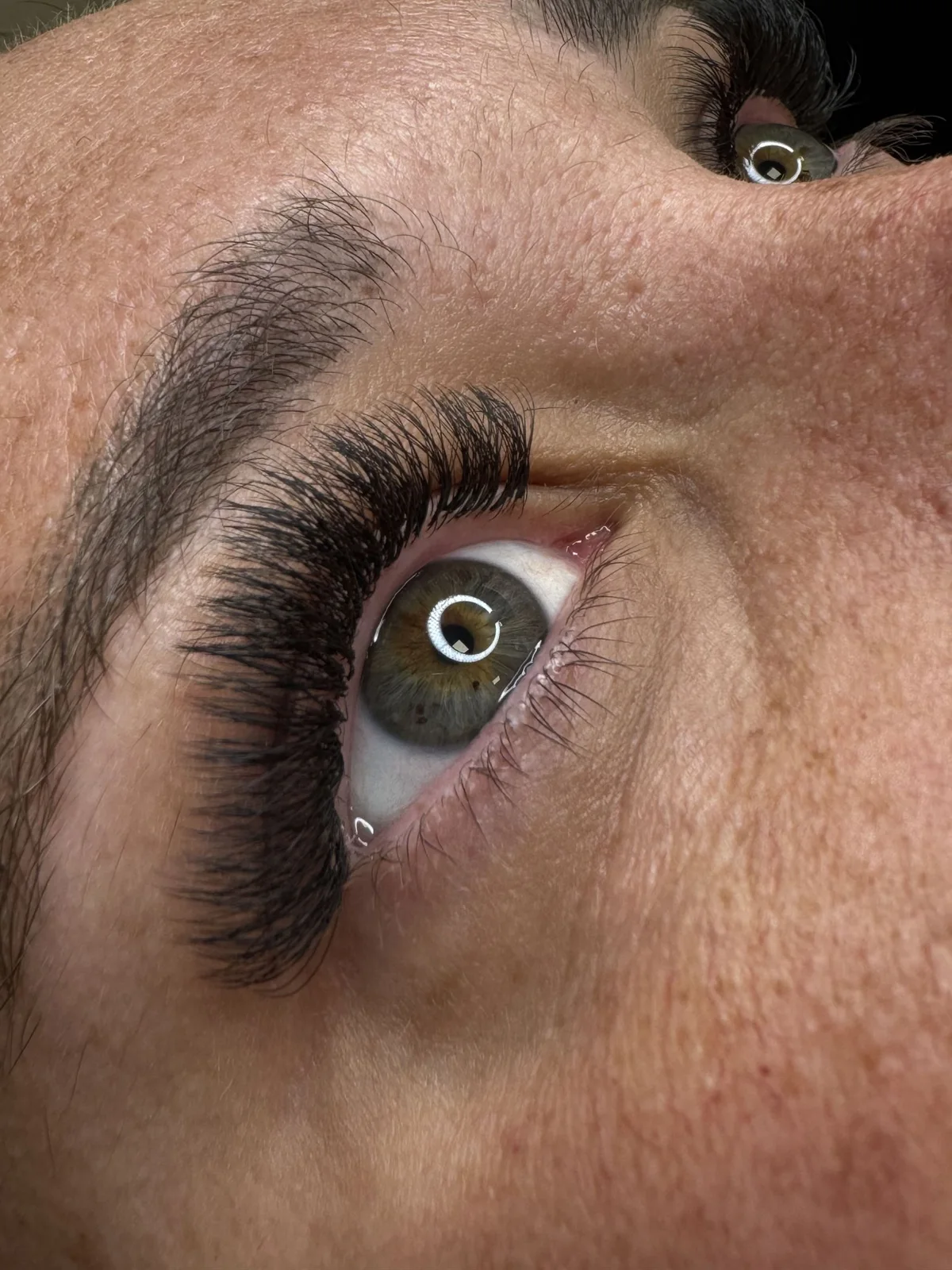 Primer plano de ojo verde con extensiones de pestañas voluminosas y ceja natural