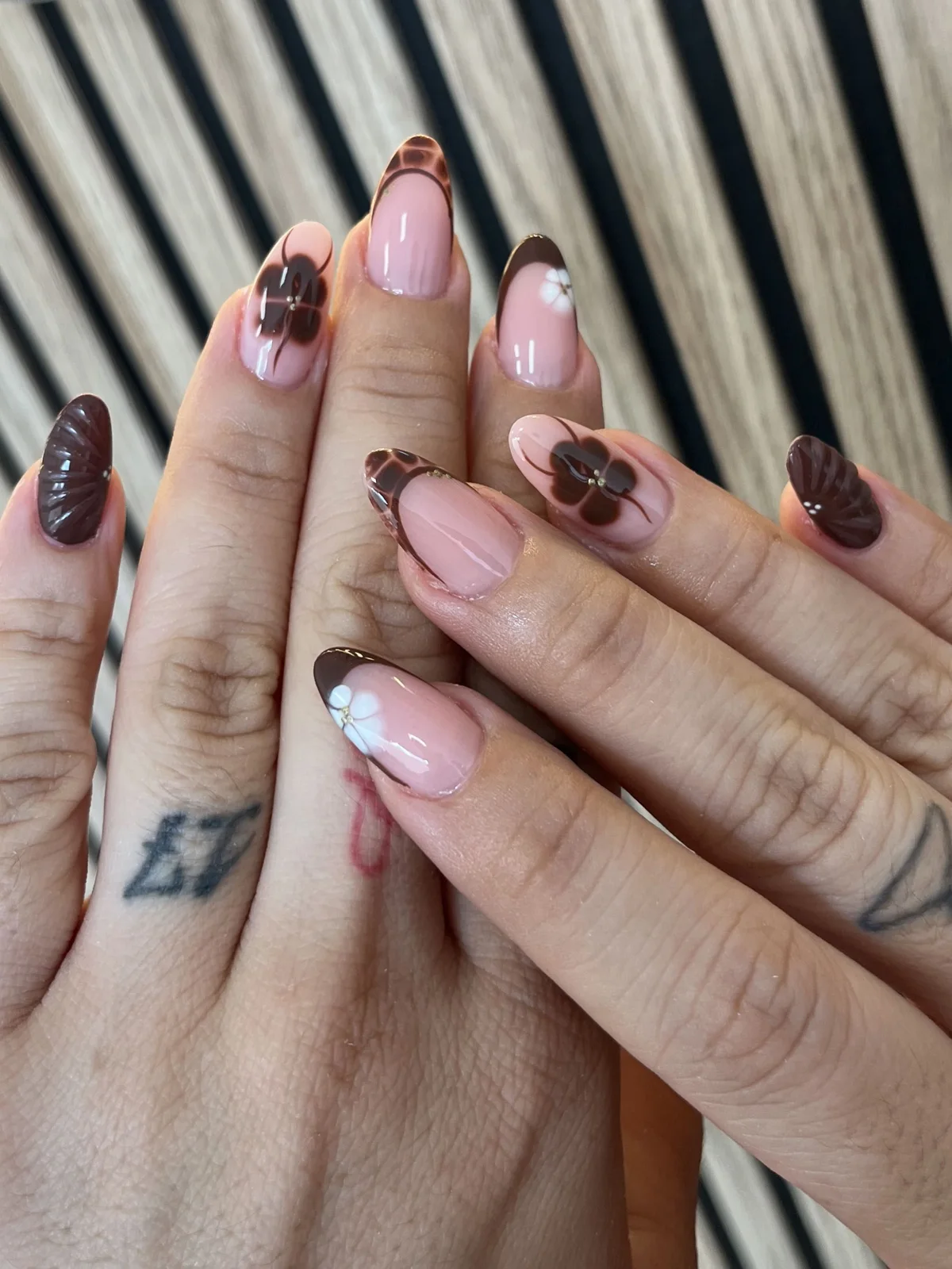 Manos con uñas almendradas rosa nude, francesa marrón chocolate y flores decoradas