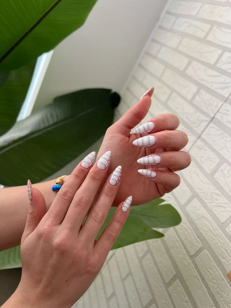 Dos manos con uñas largas almendradas blancas con líneas finas tipo cuadrícula
