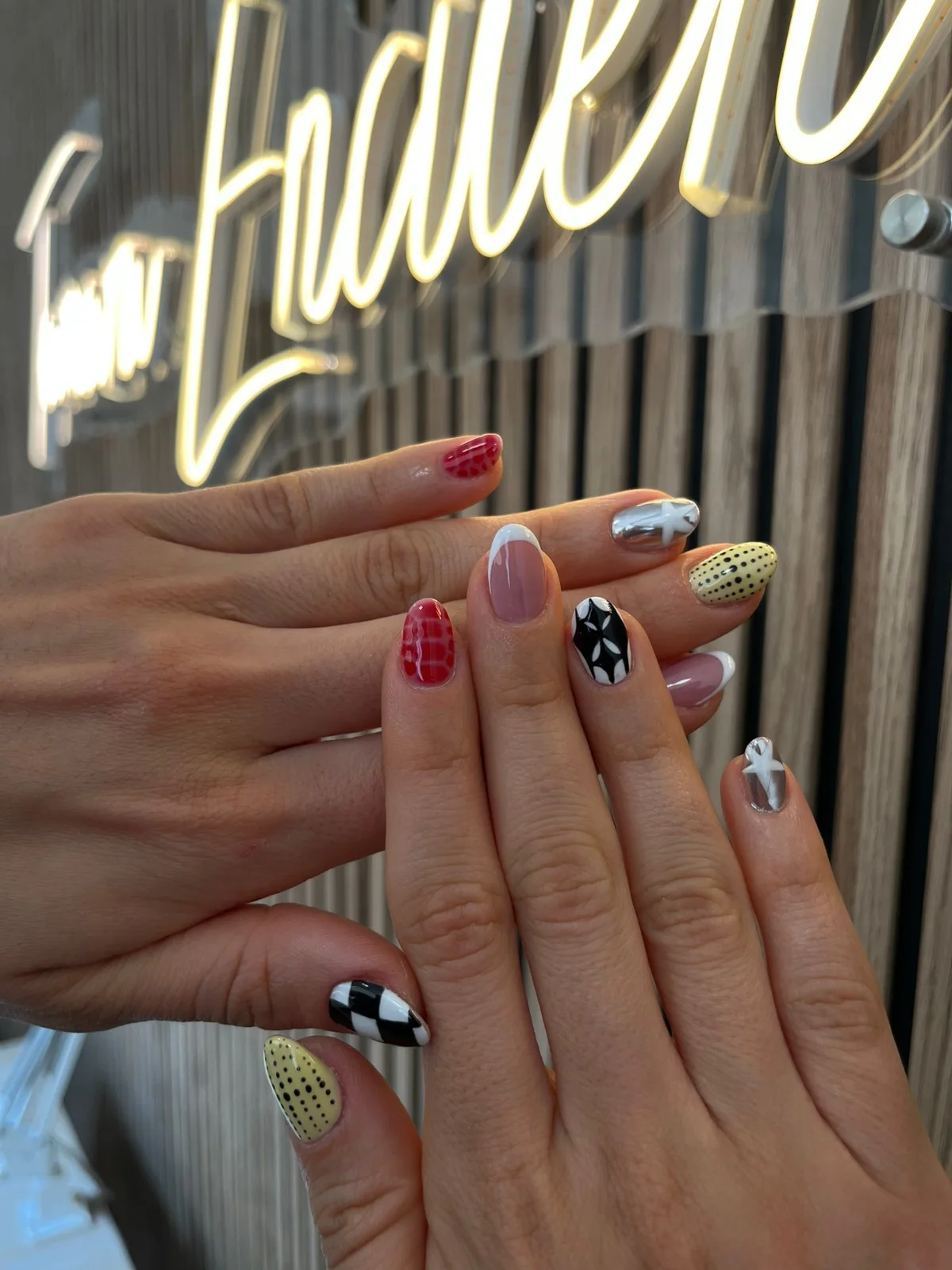 Dos manos con nail art variado: cuadros, puntos, estrellas y colores rojo, amarillo y negro