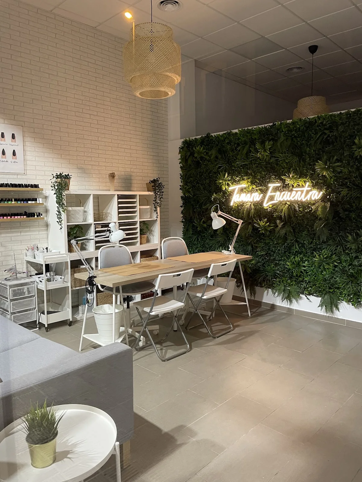 Interior del salón con pared vegetal, letrero de neón, mesa de manicura y estantería blanca