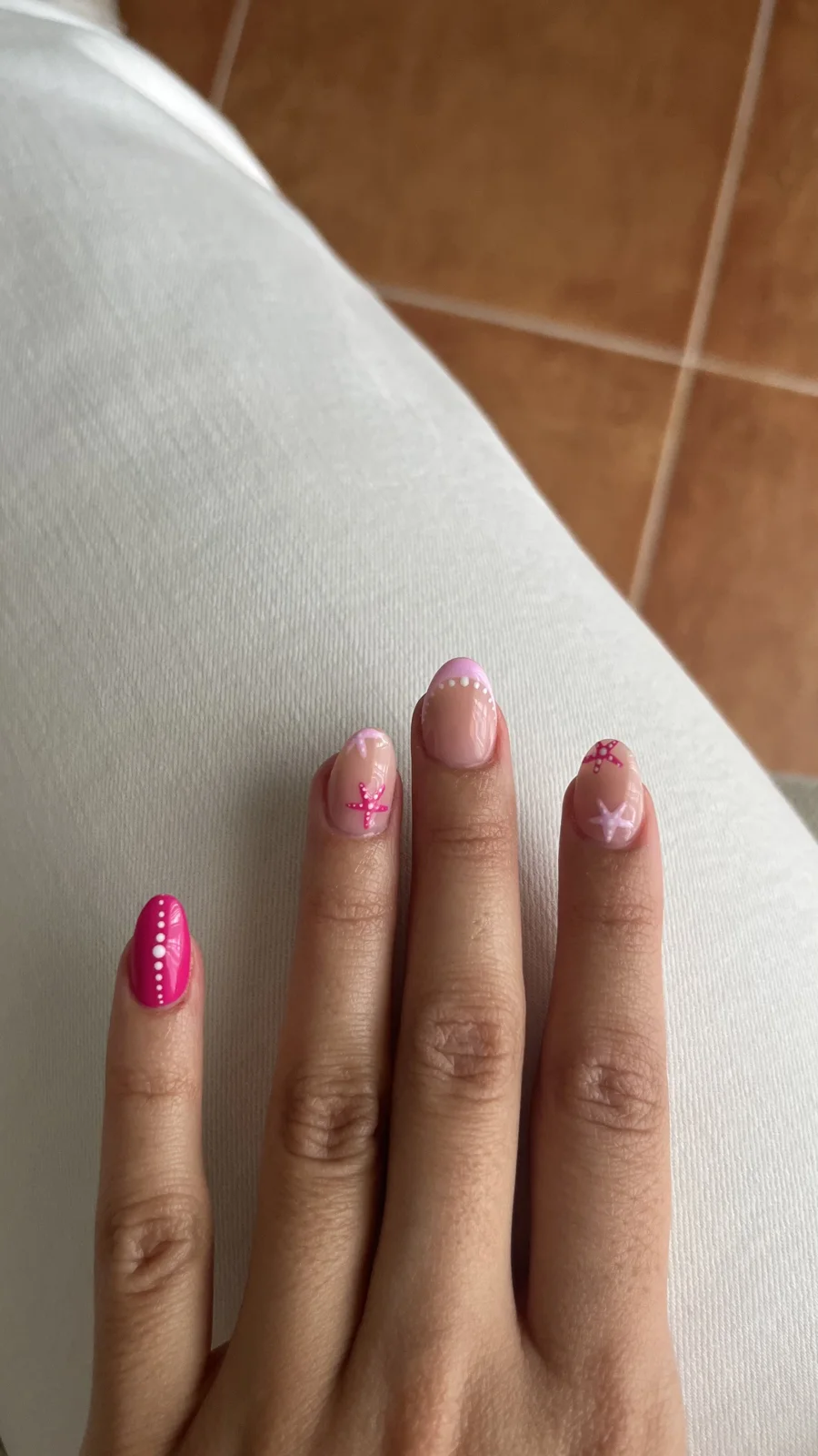 Uñas cortas con diseño rosa, puntos y estrellas de mar sobre fondo beige