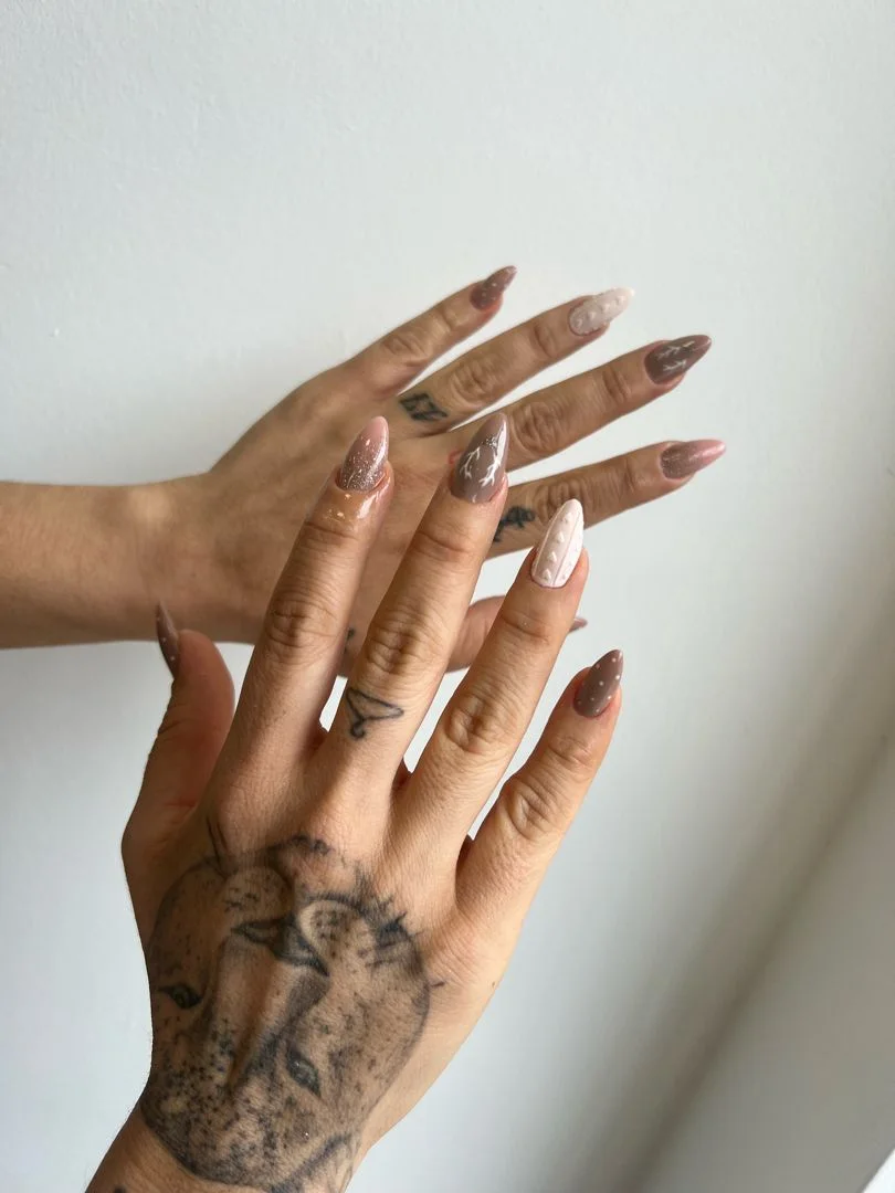 Manos con uñas almendradas en tonos nude y marrón con detalles de punto y brillo
