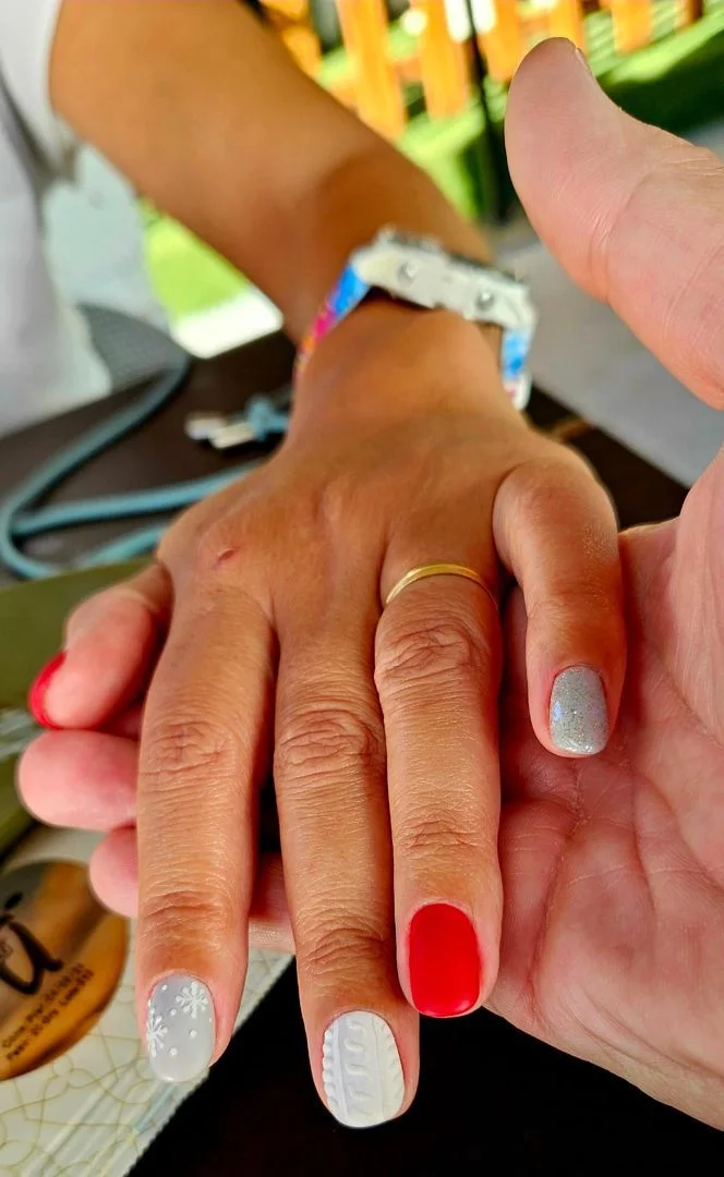 Mano con uñas navideñas rojas, plateadas y blancas con textura de punto y copos