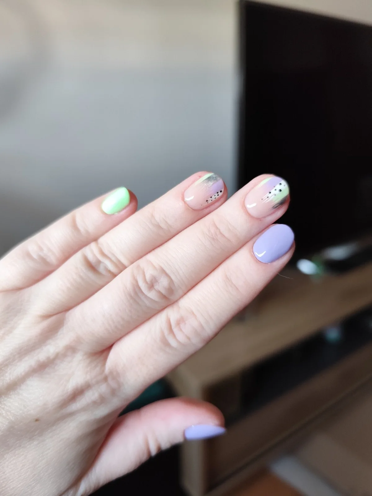 Uñas cortas en tonos pastel lila y verde con detalles abstractos y puntos negros